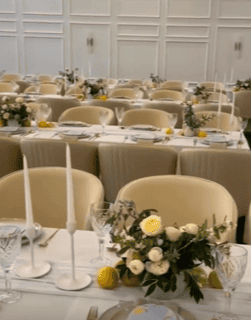 An elegant wedding setup with rows of tables adorned with cream chairs, white taper candles, and Floral Vase White Belly Pots as centerpieces. This setting beautifully illustrates the art of graceful event hire and is perfect for any occasion.
