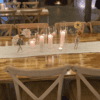 A wooden table adorned with a white runner, elegantly accentuated by glowing candles in glass holders and Floral Vase l Glass Bud arrangements, creates the perfect atmosphere for an elegant Gold Coast wedding hire event.