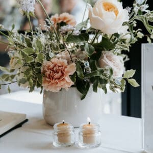 A vase of assorted flowers, including roses and carnations, sits elegantly on a table next to two small lit candles, perfect for any Gold Coast wedding hire event.