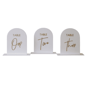 Table Numbers l White & Gold features three white, arch shaped table numbers labeled "Table One," "Table Two," and "Table Three" in elegant gold script—ideal accents for any event.