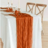 Transform your special day with an elegant white tablecloth paired with our Terracotta Cheesecloth Table Runner, complemented by plates, glasses, candles, and two wooden chairs to create a charming ambiance. Enhance your event with our Gold Coast wedding hire service for an unforgettable experience.